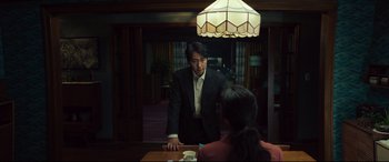 Movie still from “Decision to Leave” (2022), directed by Park Chan-wook – A man in a black suit standing in front of a woman in a red shirt; Medium shot, Over the shoulder angle