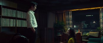 Movie still from “Decision to Leave” (2022), directed by Park Chan-wook – A man and a woman are standing in a living room; Medium shot, Low angle