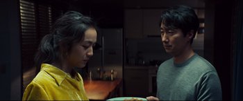 Movie still from “Decision to Leave” (2022), directed by Park Chan-wook – A man and a woman standing next to each other in front of a plate of food; Close Up shot, Over the shoulder angle