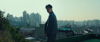 Movie still from “Decision to Leave” (2022), directed by Park Chan-wook – A man standing on top of a building looking at the camera; Medium shot, Low angle
