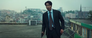 Movie still from “Decision to Leave” (2022), directed by Park Chan-wook – A man in a suit and tie holding a gun in his hand; Medium shot, Low angle