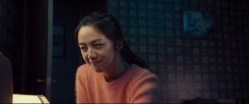 Movie still from “Decision to Leave” (2022), directed by Park Chan-wook – A woman in a pink sweater is smiling for the camera; Close Up shot, Over the shoulder angle