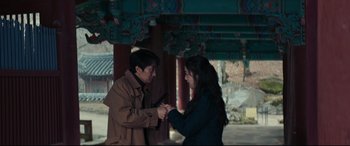 Movie still from “Decision to Leave” (2022), directed by Park Chan-wook – A man and a woman holding hands in front of a building; Medium shot, Over the shoulder angle