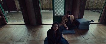 Movie still from “Decision to Leave” (2022), directed by Park Chan-wook – A woman sitting on the ground in front of a man; Wide shot, Low angle