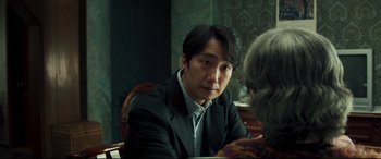 Movie still from “Decision to Leave” (2022), directed by Park Chan-wook – A man sitting at a table with an older woman; Close Up shot, Over the shoulder angle