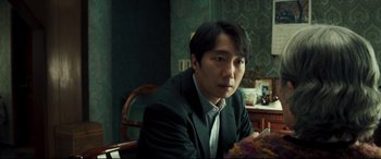 Movie still from “Decision to Leave” (2022), directed by Park Chan-wook – A man sitting in a chair in front of a table; Close Up shot, Over the shoulder angle