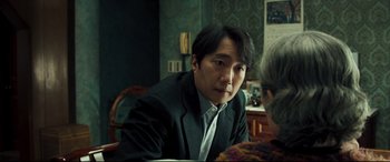 Movie still from “Decision to Leave” (2022), directed by Park Chan-wook – A man sitting at a table with another man; Close Up shot, Over the shoulder angle