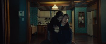Movie still from “Decision to Leave” (2022), directed by Park Chan-wook – A man and a woman are hugging in a kitchen; Medium shot, Low angle