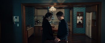 Movie still from “Decision to Leave” (2022), directed by Park Chan-wook – A man and a woman holding hands in a kitchen; Medium shot, Low angle