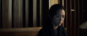 Movie still from “Decision to Leave” (2022), directed by Park Chan-wook – A woman sitting in front of a wooden wall; Close Up shot, Over the shoulder angle