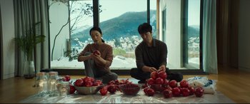 Movie still from “Decision to Leave” (2022), directed by Park Chan-wook – A man and a woman sitting in front of pomegranates on a table; Medium shot, High angle