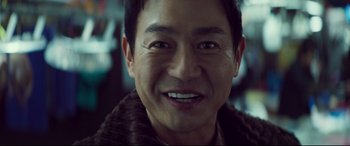 Movie still from “Decision to Leave” (2022), directed by Park Chan-wook – A man smiling for the camera; Close Up shot, Over the shoulder angle