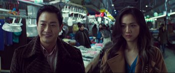 Movie still from “Decision to Leave” (2022), directed by Park Chan-wook – A man and a woman standing next to each other in a market; Close Up shot, Over the shoulder angle