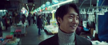 Movie still from “Decision to Leave” (2022), directed by Park Chan-wook – A man standing in front of a group of people; Close Up shot, Over the shoulder angle
