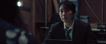 Movie still from “Decision to Leave” (2022), directed by Park Chan-wook – A man wearing a suit and tie sitting in front of a computer; Close Up shot, Over the shoulder angle