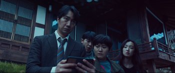 Movie still from “Decision to Leave” (2022), directed by Park Chan-wook – A group of people standing next to each other looking at a cell phone; Medium shot, Low angle