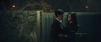Movie still from “Decision to Leave” (2022), directed by Park Chan-wook – A man and a woman standing next to each other in front of a stone wall; Medium shot, Low angle