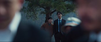 Movie still from “Decision to Leave” (2022), directed by Park Chan-wook – Two men standing next to each other under a tree; Medium shot, Over the shoulder angle