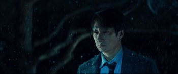 Movie still from “Decision to Leave” (2022), directed by Park Chan-wook – A man wearing a suit and tie standing in front of a tree; Close Up shot, Low angle