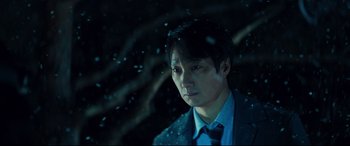 Movie still from “Decision to Leave” (2022), directed by Park Chan-wook – A man wearing a suit and tie standing in front of a tree; Close Up shot, Over the shoulder angle