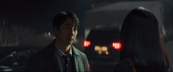 Movie still from “Decision to Leave” (2022), directed by Park Chan-wook – A man standing next to a car on a street; Close Up shot, Over the shoulder angle