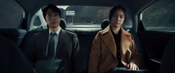 Movie still from “Decision to Leave” (2022), directed by Park Chan-wook – A man and a woman sitting in the back of a car; Medium shot, Over the shoulder angle