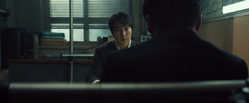 Movie still from “Decision to Leave” (2022), directed by Park Chan-wook – A man sitting at a table in front of another man; Close Up shot, Over the shoulder angle