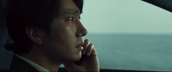Movie still from “Decision to Leave” (2022), directed by Park Chan-wook – A person sitting in a car with his hand under his chin; Close Up shot, Low angle