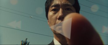 Movie still from “Decision to Leave” (2022), directed by Park Chan-wook – A man's face with a paper airplane in his mouth; Extreme Close Up shot, Low angle