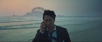 Movie still from “Decision to Leave” (2022), directed by Park Chan-wook – A man on a cell phone on the beach; Medium shot, Low angle