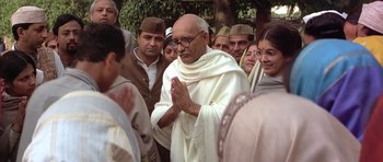 Movie still from “Gandhi” (1982), directed by Richard Attenborough – An old man in a white robe is praying with a group of people; Medium shot, Over the shoulder angle