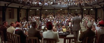 Movie still from “Gandhi” (1982), directed by Richard Attenborough – A group of people sitting in front of an audience; Extreme Wide shot, High angle