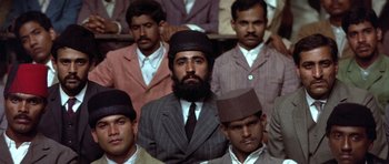 Movie still from “Gandhi” (1982), directed by Richard Attenborough – A group of men in suits and hats sitting in a row; Medium shot, High angle