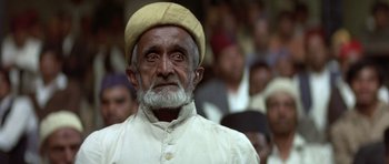 Movie still from “Gandhi” (1982), directed by Richard Attenborough – An old man with a beard wearing a white hat; Close Up shot, Low angle