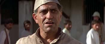 Movie still from “Gandhi” (1982), directed by Richard Attenborough – An old man wearing a white hat and a brown shirt; Close Up shot, Low angle