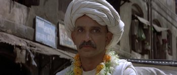 Movie still from “Gandhi” (1982), directed by Richard Attenborough – A man wearing a white turban and a flower necklace; Close Up shot, Low angle