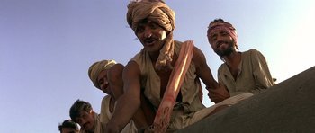 Movie still from “Gandhi” (1982), directed by Richard Attenborough – A group of men sitting next to each other on top of a building; Medium shot, Low angle