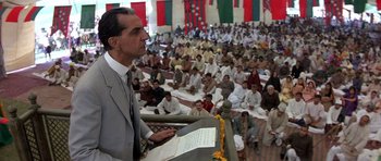 Movie still from “Gandhi” (1982), directed by Richard Attenborough – A man in a gray suit giving a speech to a crowd of people; Medium shot, Low angle