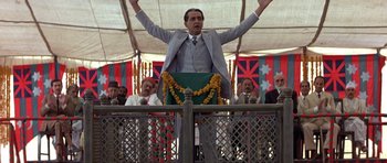 Movie still from “Gandhi” (1982), directed by Richard Attenborough – A man in a gray suit is holding his hands up; Medium shot, Low angle