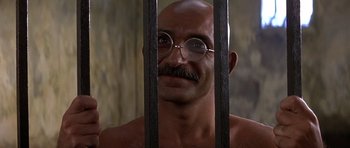 Movie still from “Gandhi” (1982), directed by Richard Attenborough – A bald man with glasses and a mustache behind bars; Close Up shot, Low angle