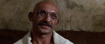 Movie still from “Gandhi” (1982), directed by Richard Attenborough – A bald man with glasses and a mustache wearing a white robe; Close Up shot, Over the shoulder angle