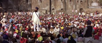 Movie still from “Gandhi” (1982), directed by Richard Attenborough – A crowd of people sitting and standing around a man in a turban; Wide shot, High angle