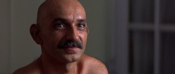 Movie still from “Gandhi” (1982), directed by Richard Attenborough – A bald man with a mustache is looking at the camera; Close Up shot, Over the shoulder angle
