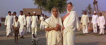 Movie still from “Gandhi” (1982), directed by Richard Attenborough – A couple of women standing next to each other on a dirt road; Medium shot, Low angle