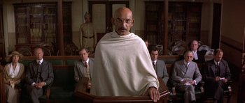 Movie still from “Gandhi” (1982), directed by Richard Attenborough – An old man with a beard and a white robe is in a court room; Medium shot, Low angle