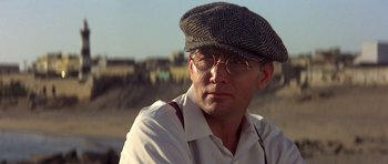 Movie still from “Gandhi” (1982), directed by Richard Attenborough – A man wearing glasses and a hat is looking at the camera; Close Up shot, Low angle
