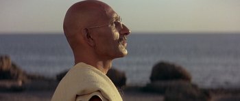 Movie still from “Gandhi” (1982), directed by Richard Attenborough – A bald man wearing glasses and a white shirt; Close Up shot, Low angle