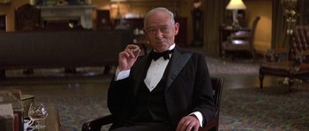 Movie still from “Gandhi” (1982), directed by Richard Attenborough – An older man in a tuxedo sitting in a chair holding a cell phone to his ear; Medium shot, Low angle