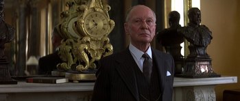 Movie still from “Gandhi” (1982), directed by Richard Attenborough – An older man wearing a suit and tie in front of a clock; Close Up shot, Low angle