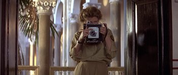 Movie still from “Gandhi” (1982), directed by Richard Attenborough – A woman holding an old camera in front of her face; Medium shot, Over the shoulder angle